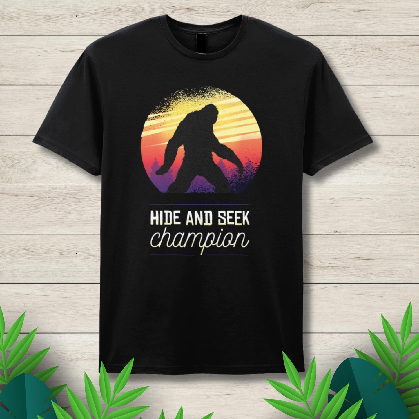 Black t-shirt with a 'Hide and Seek Champion' design featuring a silhouette of a person and a colorful sunset on a wooden background.