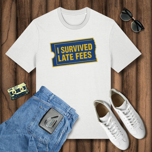 White t-shirt with 'I Survived Late Fees' design, blue jeans, white sneakers, and sunglasses on a wooden surface.