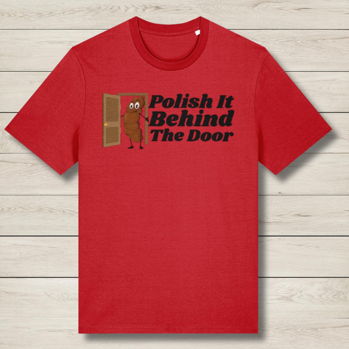 Red t-shirt with cartoon character and text 'Polish It Behind The Door' on a wooden surface