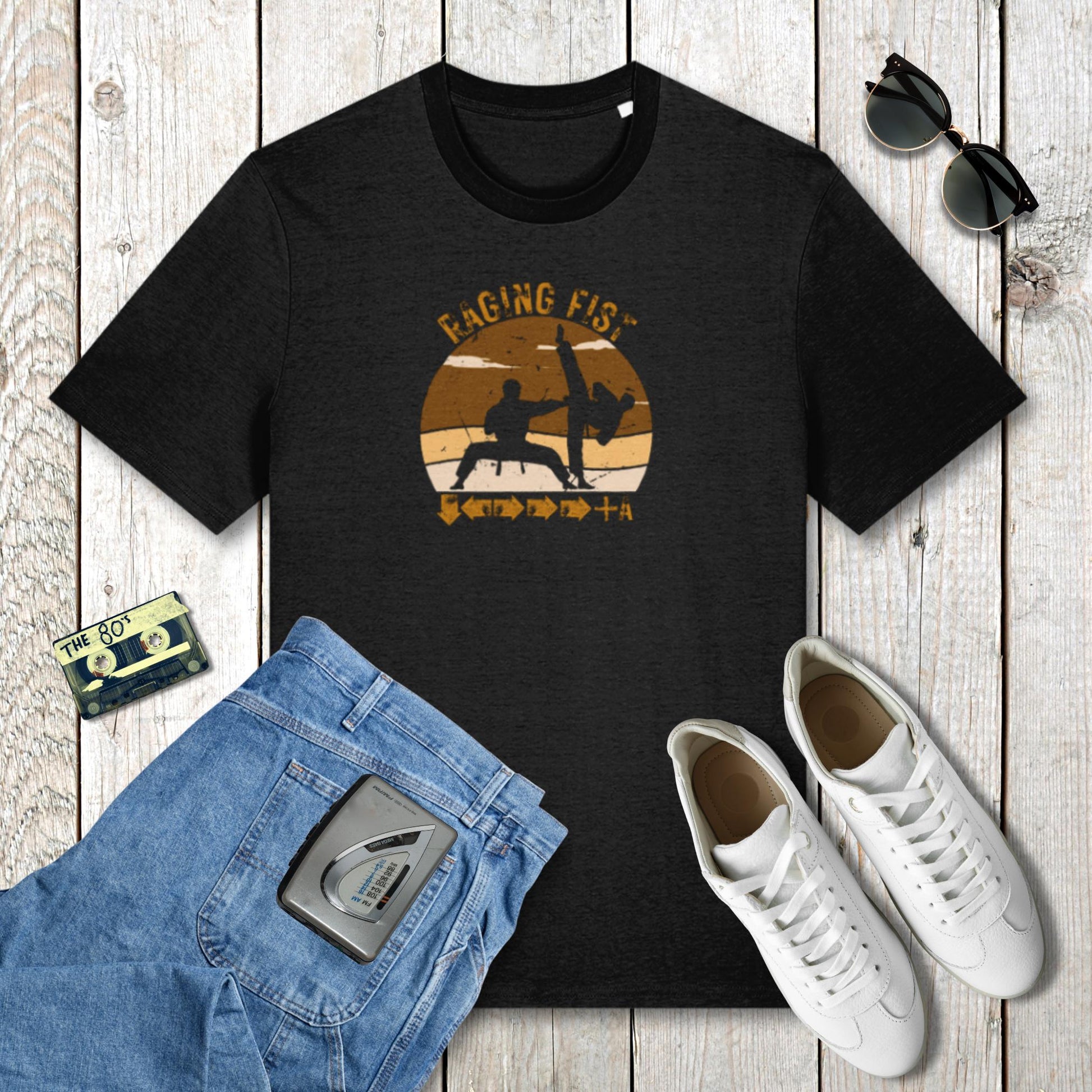Black t-shirt with graphic design on a wooden surface with jeans, sneakers, and sunglasses.