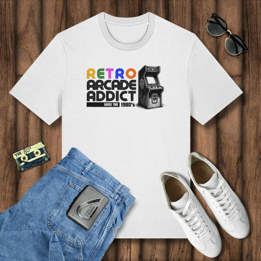 White t-shirt with 'Retro Arcade Addict' design on a wooden surface with jeans, sneakers, and a cassette tape.