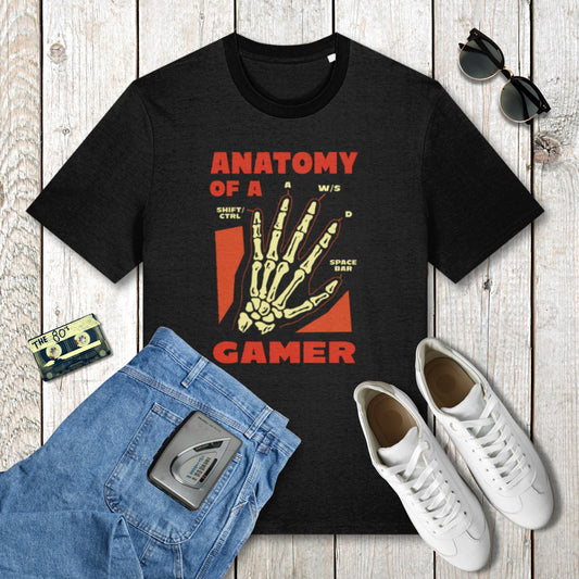 Black t-shirt with 'Anatomy of a Gamer' design on a wooden surface with jeans, sneakers, and a cassette tape.
