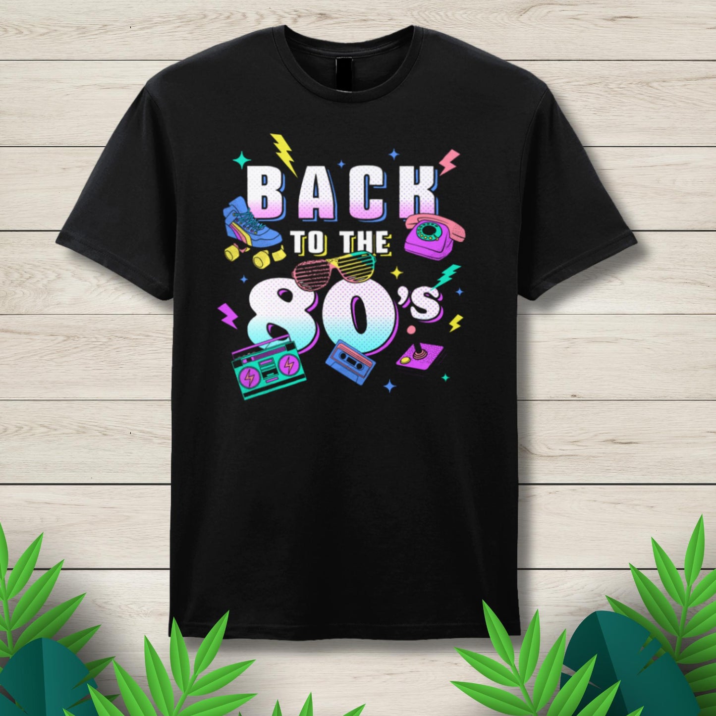 Black t-shirt with 'Back to the 80's' design on a wooden surface with decorative leaves.
