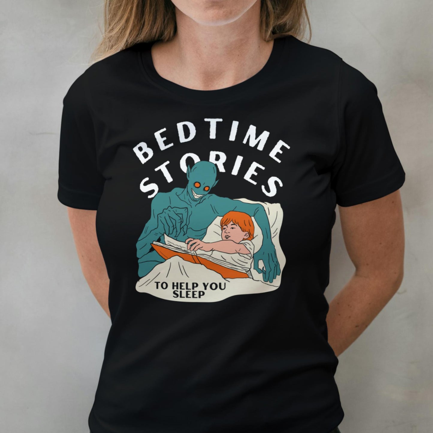 Person wearing a black t-shirt with a graphic design of a blue creature reading to a child, accompanied by the text 'Bedtime Stories to Help You Sleep'.