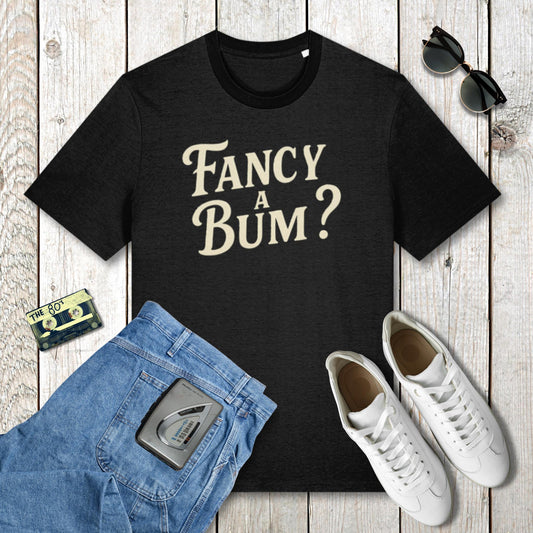 Black t-shirt with 'Fancy A Bum?' text, blue jeans, white sneakers, and sunglasses on a wooden surface.
