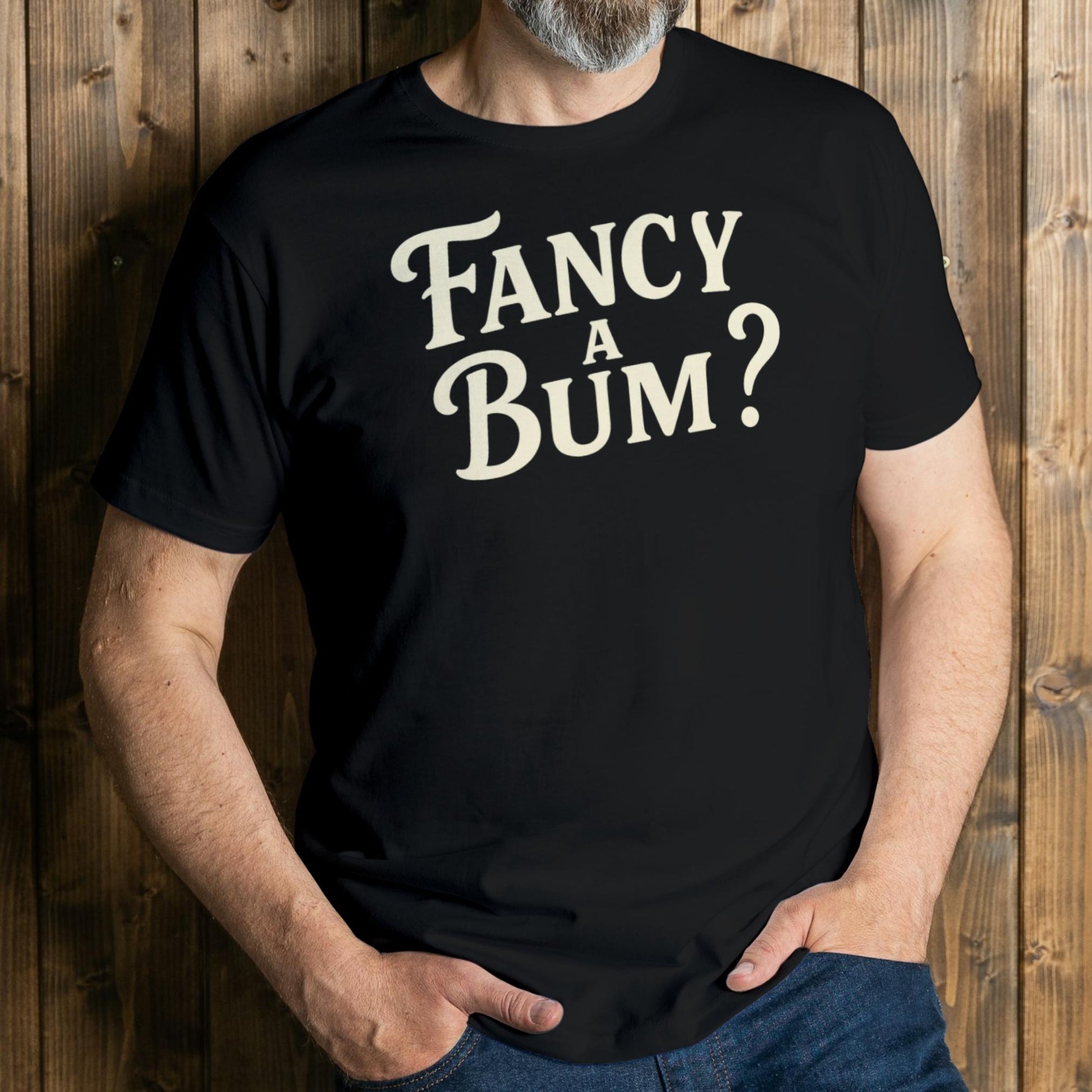Person wearing a black t-shirt with 'Fancy A Bum?' text against a wooden background
