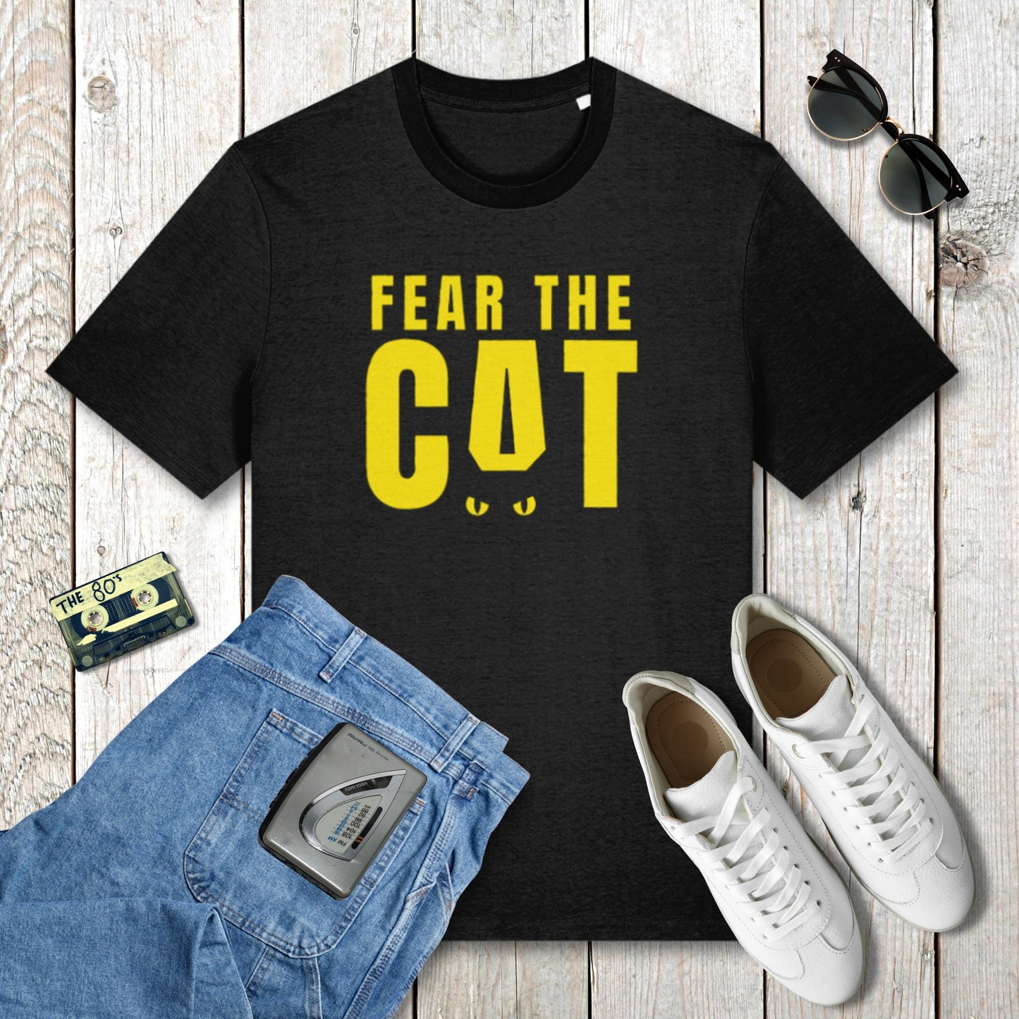 Black t-shirt with 'Fear the Cat' text, blue jeans, white sneakers, and sunglasses on a wooden surface.