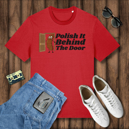 Red t-shirt with 'Polish It Behind The Door' graphic on a wooden surface with jeans, sneakers, and sunglasses.