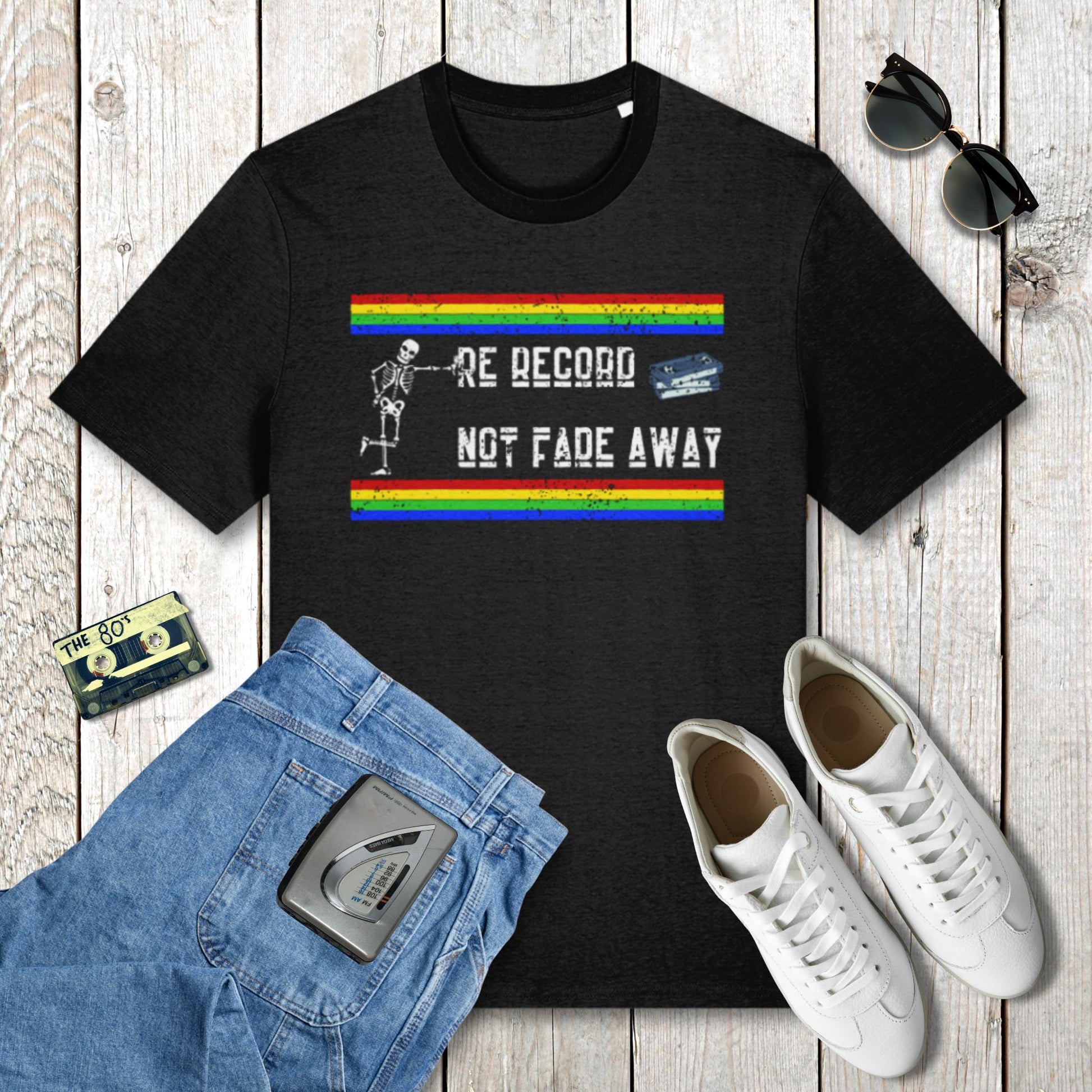Black t-shirt with colorful graphic and text on a wooden surface with jeans, sneakers, and sunglasses.