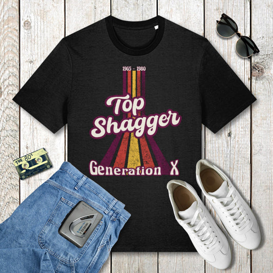 Black t-shirt with 'Top Shagger Generation X' design on a wooden surface with jeans, sneakers, and a cassette tape.