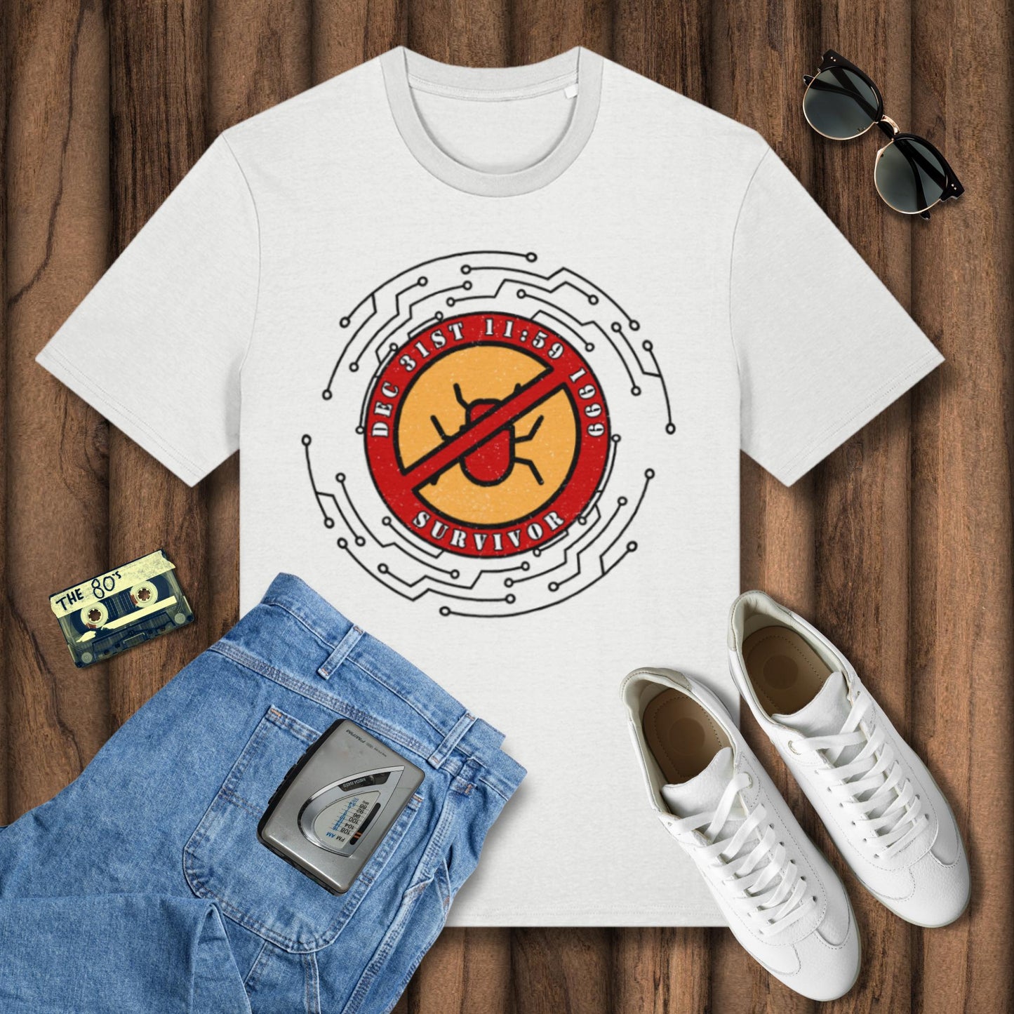 White t-shirt with graphic design on a wooden surface, surrounded by jeans, sneakers, sunglasses, and a cassette tape.
