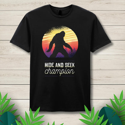 Black t-shirt with a 'Hide and Seek Champion' design featuring a silhouette of a person and a colorful sunset on a wooden background.