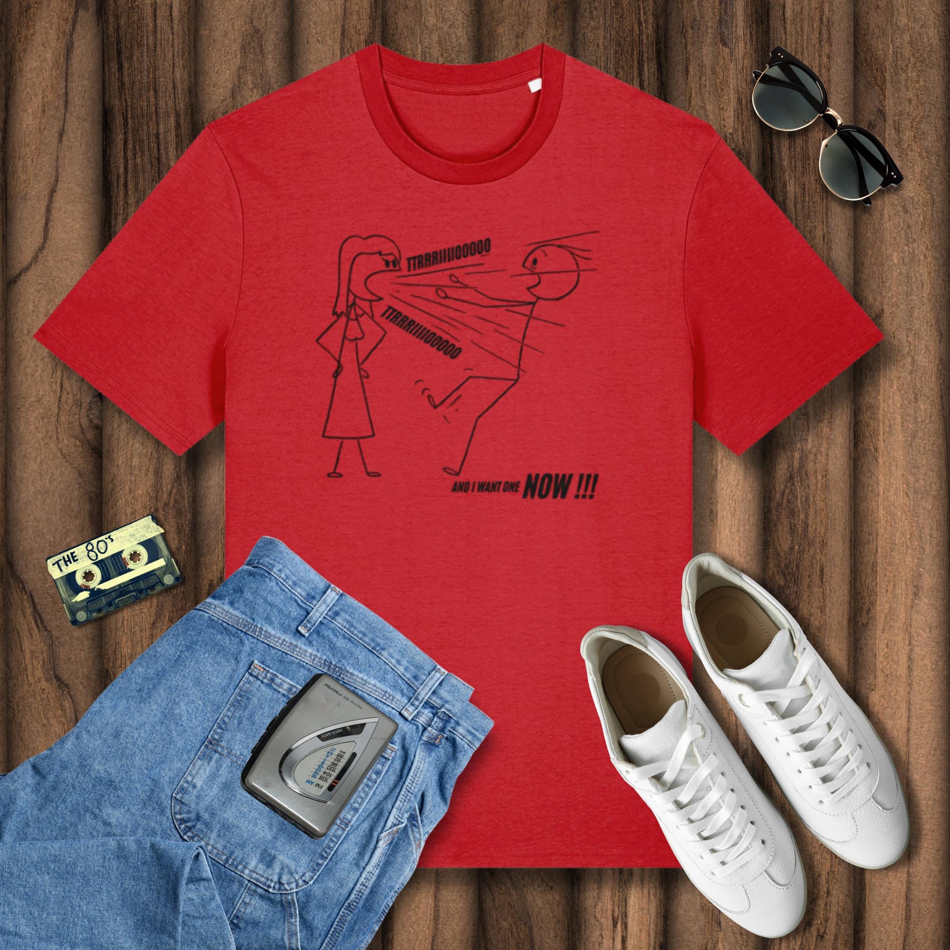 Red t-shirt with graphic design, blue jeans, white sneakers, sunglasses, and a cassette tape on a wooden surface.