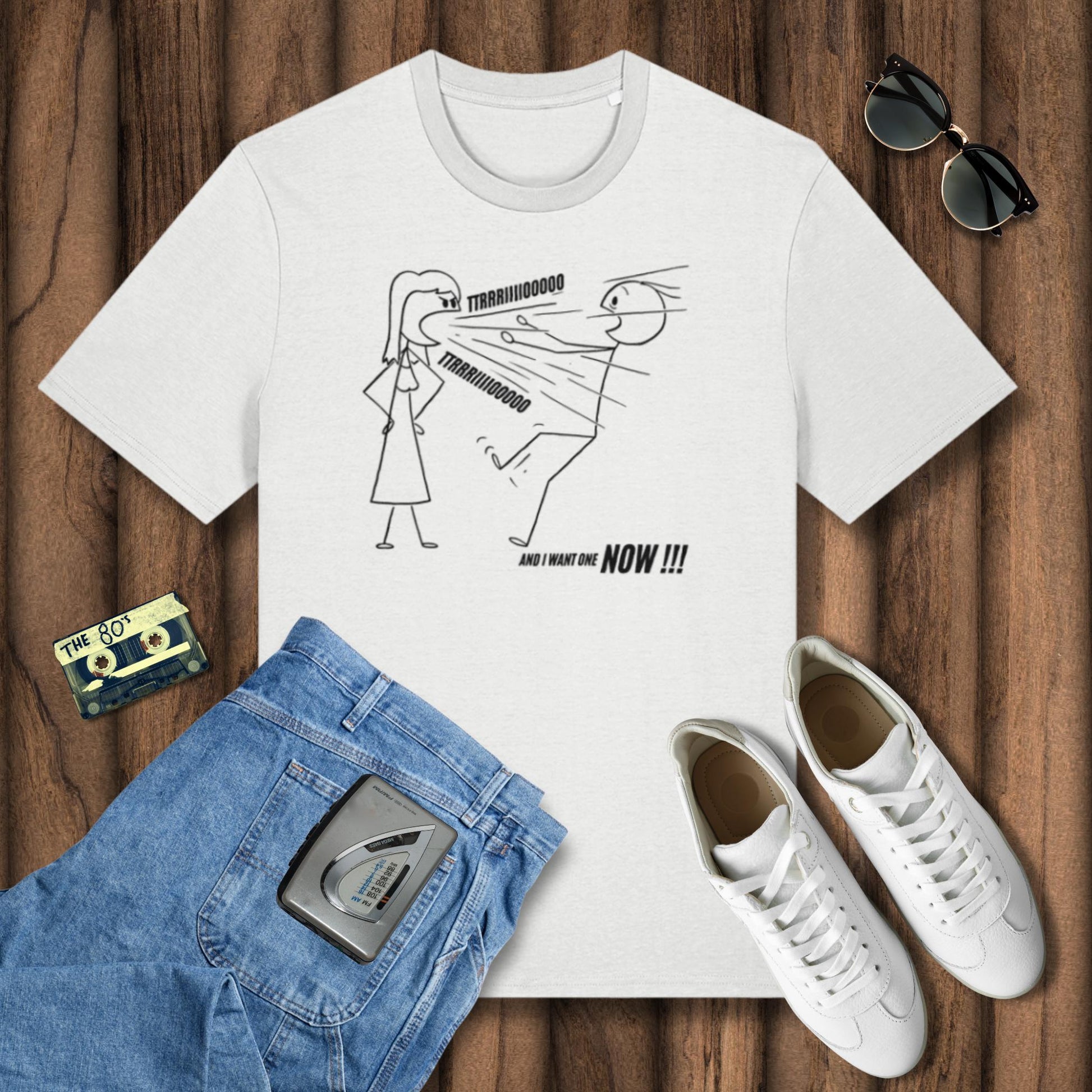 White t-shirt with graphic design, blue jeans, white sneakers, and sunglasses on a wooden surface.