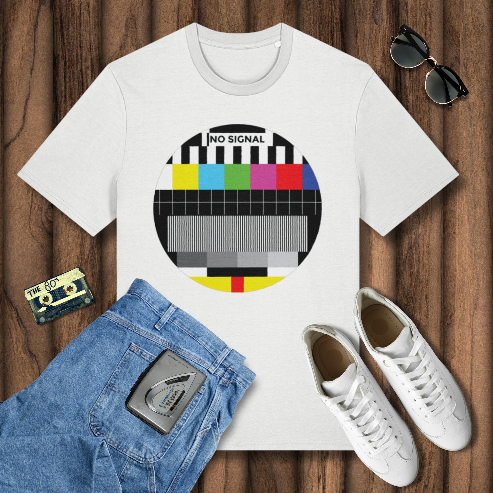 White t-shirt with TV test pattern design, sunglasses, jeans, cassette tape, and sneakers on a wooden surface