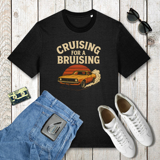 Black t-shirt with 'Cruising for a Bruising' graphic on a wooden surface with jeans, sneakers, and sunglasses.