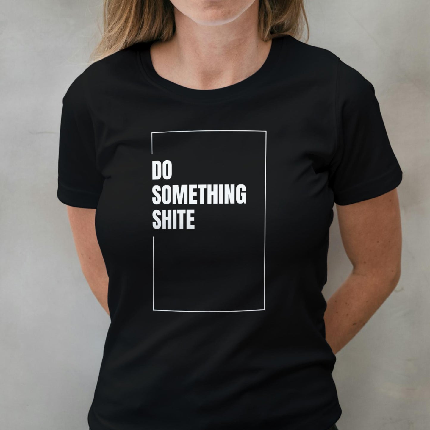 Person wearing a black t-shirt with white text 'DO SOMETHING SHITE' on a plain background