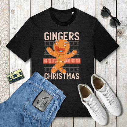 Black t-shirt with gingerbread man graphic and text on a wooden surface with jeans, sneakers, and sunglasses.