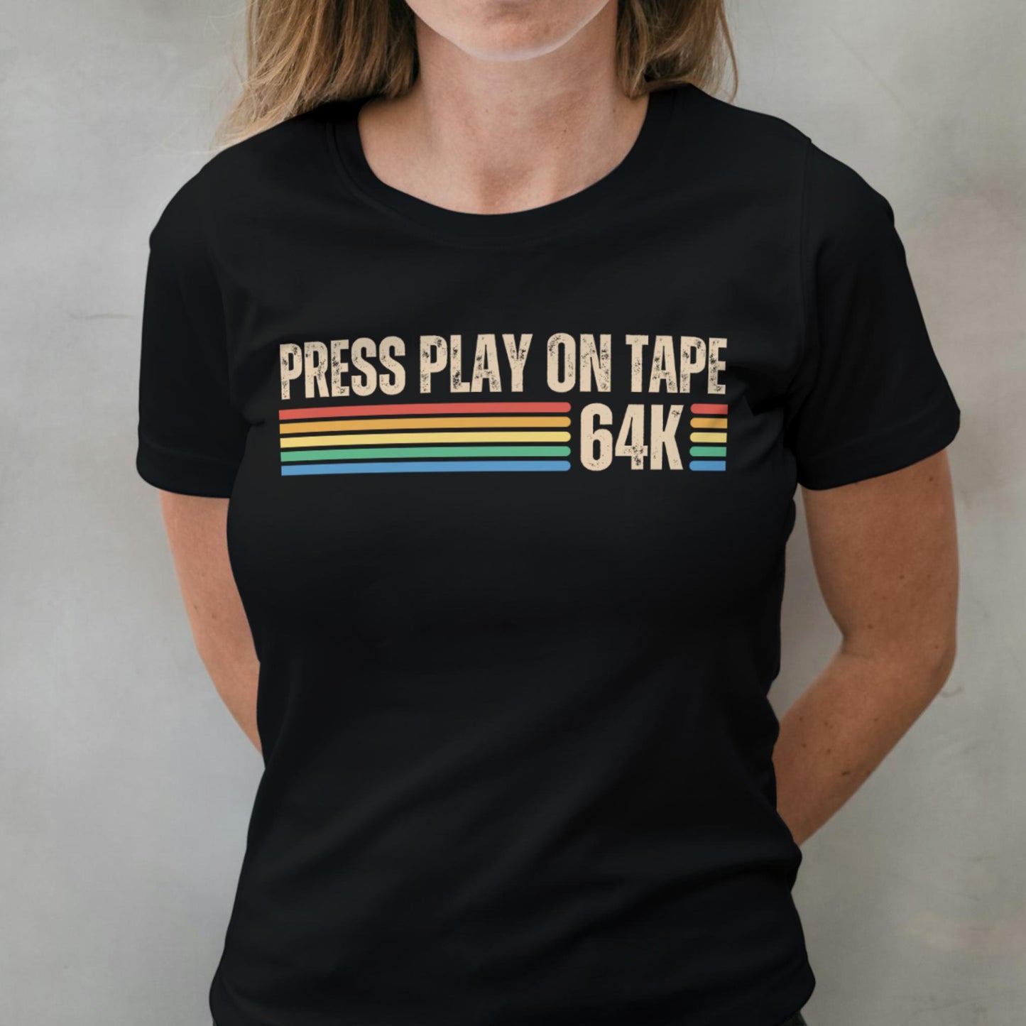 Person wearing a black t-shirt with 'Press Play on Tape 64K' text and colorful stripes.