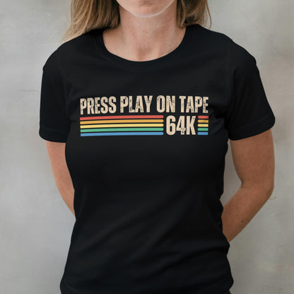 Person wearing a black t-shirt with 'Press Play on Tape 64K' text and colorful stripes.