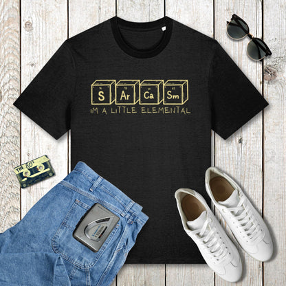 Black t-shirt with 'Sarcasm is a Little Elemental' text, blue jeans, white sneakers, and sunglasses on a wooden surface.