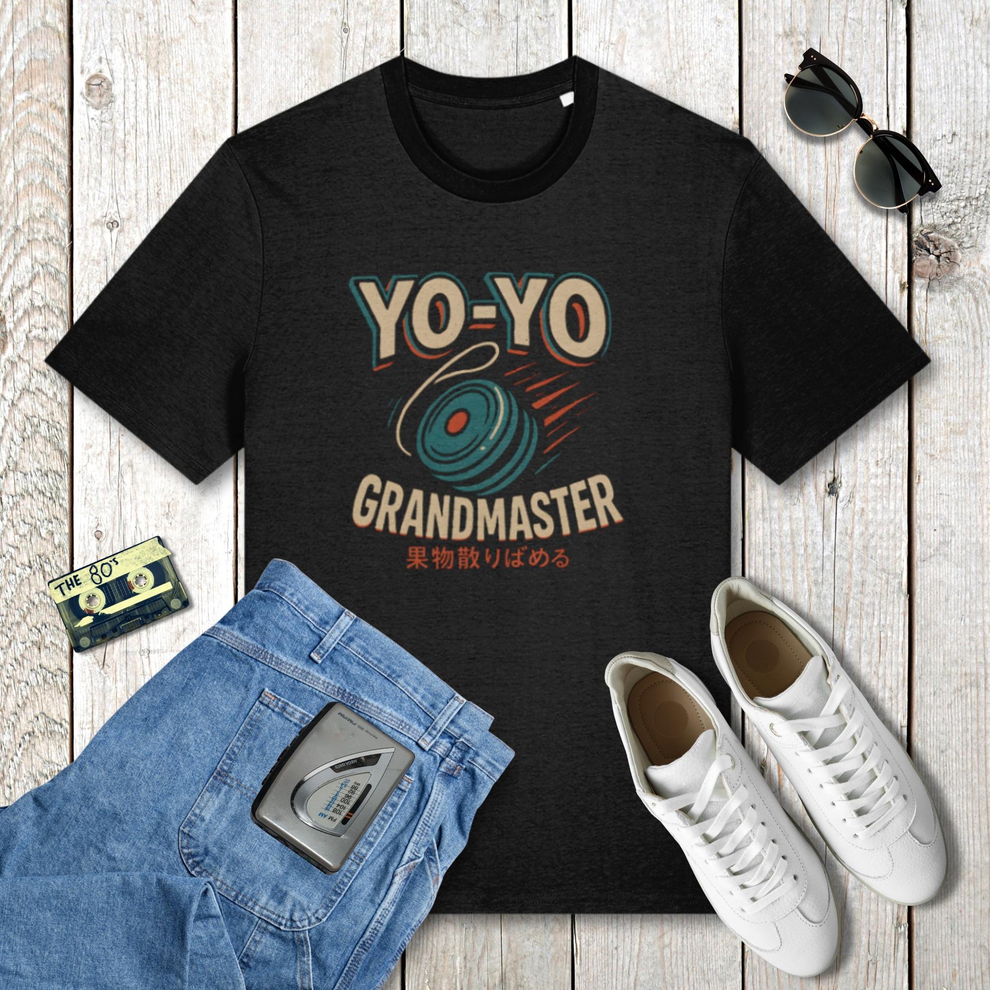 Black t-shirt with 'YO-YO Grandmaster' design on a wooden surface with jeans, sneakers, and a cassette tape.