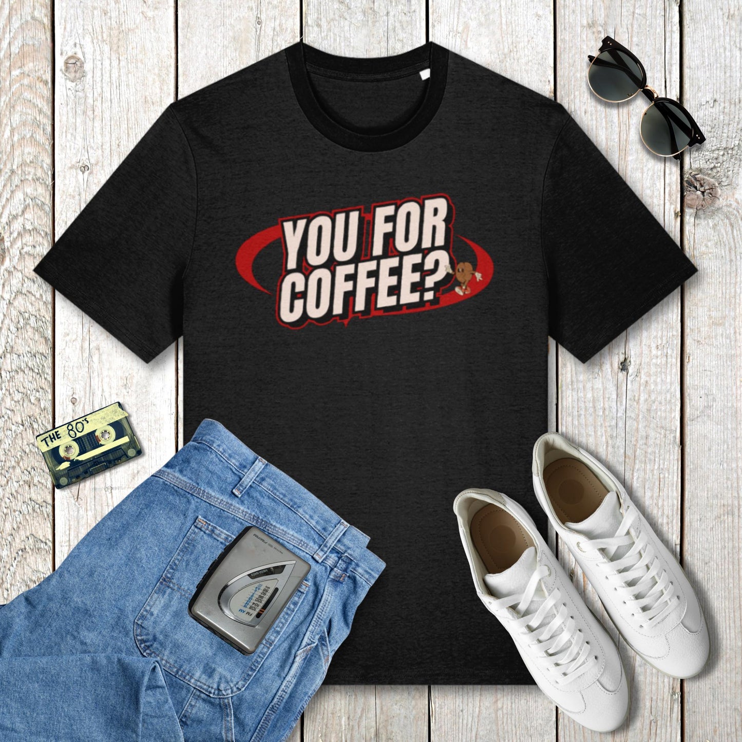 Black t-shirt with 'YOU FOR COFFEE?' text, blue jeans, white sneakers, and sunglasses on a wooden surface.